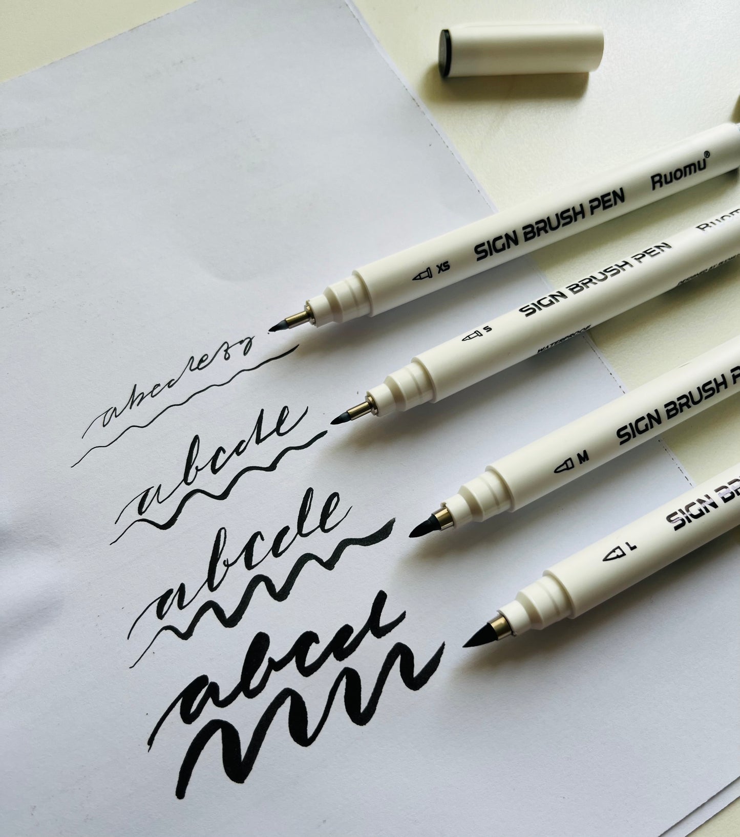 Three SICN BRUSH PEN markers on a piece of paper with calligraphy practice.