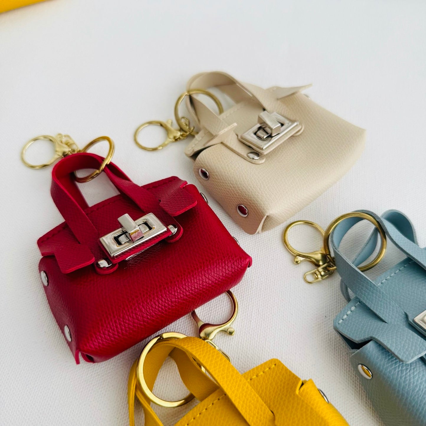 Set of miniature leather handbags in red, beige, yellow, and blue on a white background