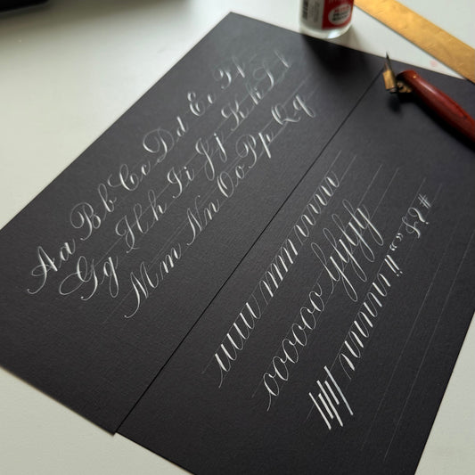 Calligraphy practice sheet with pen and ink bottle on a table