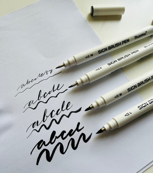 Three SICN BRUSH PEN markers on a piece of paper with calligraphy practice.