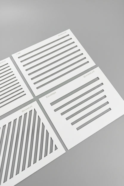White stencil sheets with black linear patterns laid out on a black textured surface.